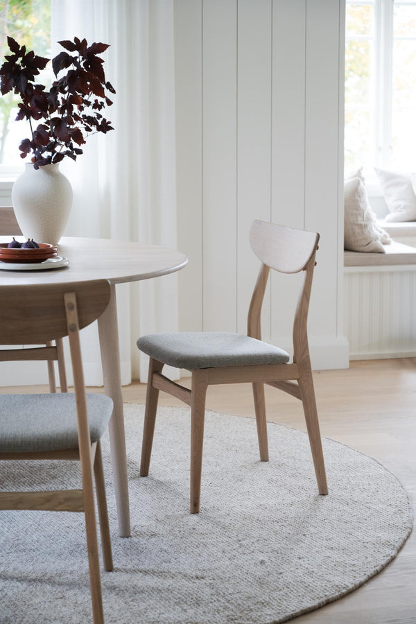 Ljus trämatstol med grå stoppad sits vid runt matbord i skandinavisk stil