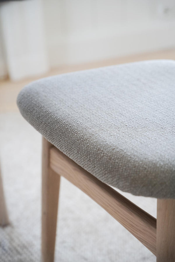 Grå stoppad stol med träben i ljust trä, närbild på sits och detaljer i skandinavisk design