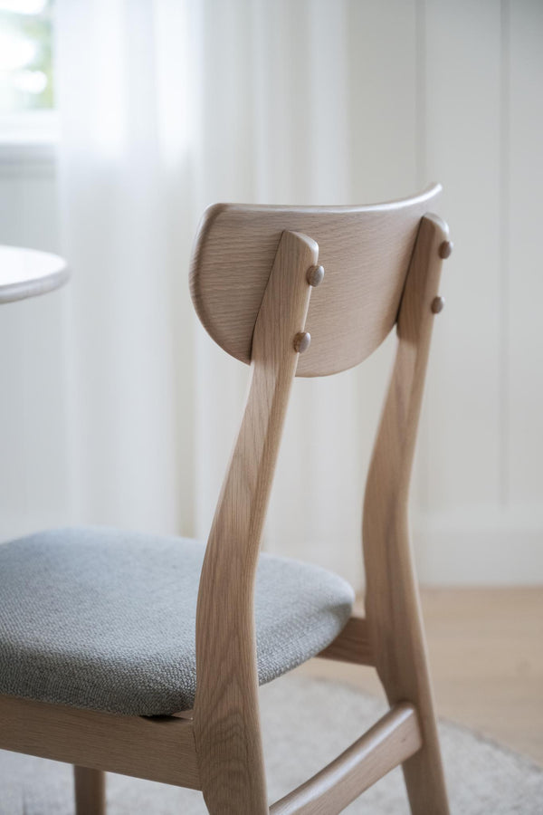 Närbild av ljus träfåtölj med grå stoppning och elegant ryggstöd i skandinavisk design