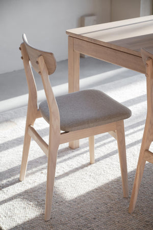Matstol i ljust trä med grå klädsel och rundad rygg vid matbord i skandinavisk design