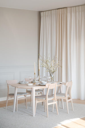 Ljus matplats med runt matbord i ljust trä, matchande stolar och beige gardin i skandinavisk stil
