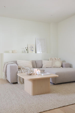 Ljust vardagsrum med grå soffa, ljust träsoffbord, beige textilier och minimalistisk inredning i neutrala toner