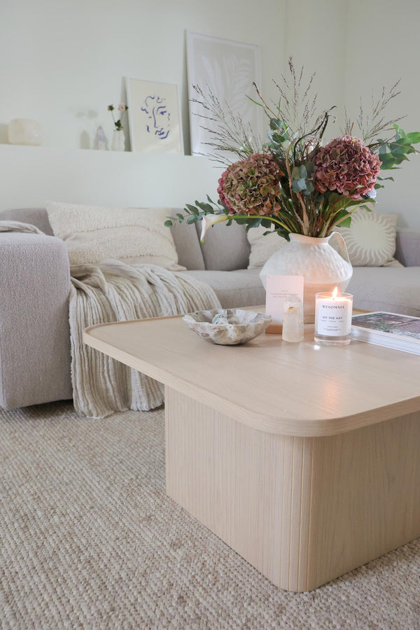 Ljust vardagsrum med beige soffbord, vita ljus, vas med torkade blommor och minimalistisk inredning