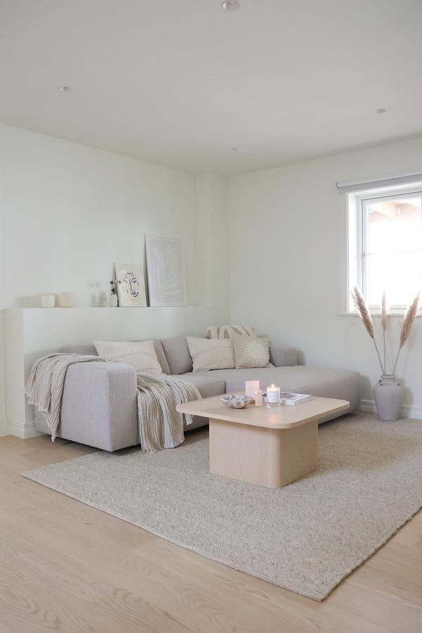 Ljust vardagsrum med grå soffa, beige soffbord, krämfärgad matta och pampagräs i vas