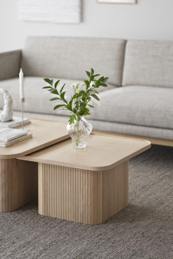 Soffbord i ljust trä med räfflad kant, dekorerat med vas och böcker framför grå soffa