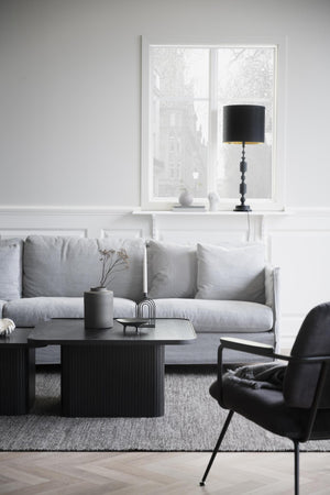 Minimalistiskt vardagsrum med grå soffa, svart soffbord och elegant lampa i fönstret