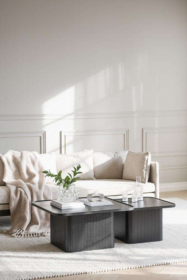 Modernt soffbord i mörkt trä med räfflad design, dekorerat med böcker, vas och ljus i ljust vardagsrum