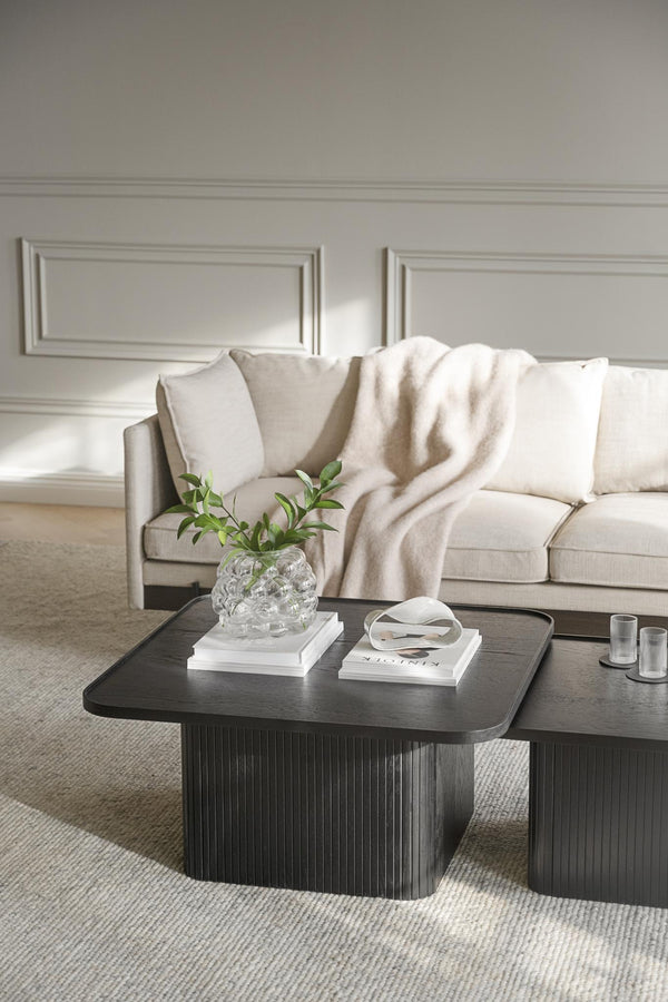 Elegant soffbord i mörkt trä med räfflad kant framför beige soffa med kuddar och pläd i ljust vardagsrum