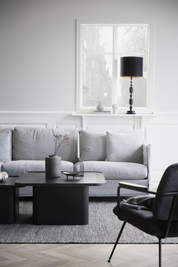 Ljusgrå soffa med soffbord i svart trä och elegant fåtölj i modern skandinavisk vardagsrumsinredning