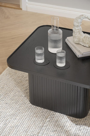 Svart soffbord med räfflad design, dekorerat med glaskaraff och glas på beige matta