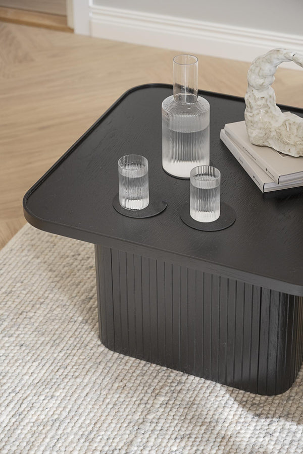 Svart soffbord med räfflad design, dekorerat med glaskaraff och glas på beige matta