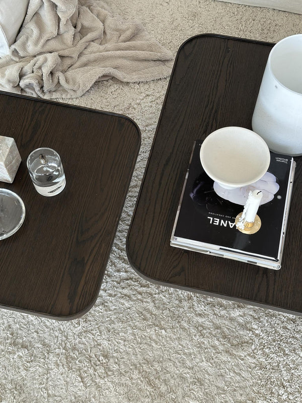 Soffbord i mörkt trä med böcker, vas och glas på ljus matta i vardagsrumsmiljö