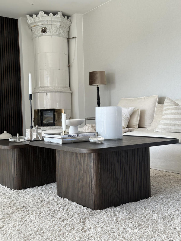 Mörkbrunt soffbord med räfflad design i vardagsrum med vit kakelugn och beige soffa