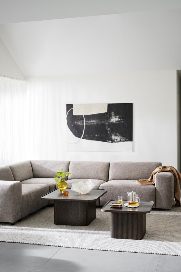 Grå hörnsoffa med soffbord i mörkt trä i minimalistiskt vardagsrum med abstrakt konst på väggen