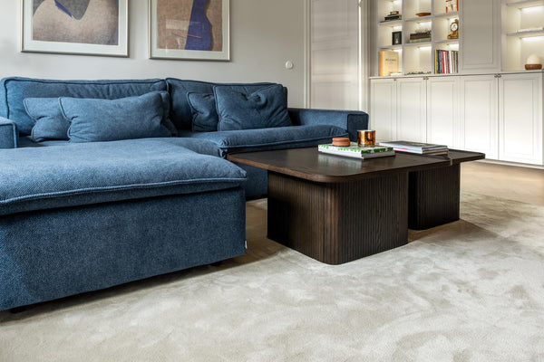 Blå sammetssoffa med mörkt träsoffbord på ljus matta i modernt vardagsrum med bokhylla