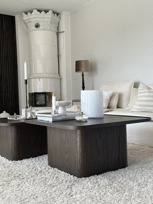 Mörkt soffbord i trä med räfflad design, stylat med ljus, böcker och dekoration i ljust vardagsrum