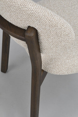 Närbild av en stol med cremefärgad stickad klädsel och mörkbruna träben i rustik finish