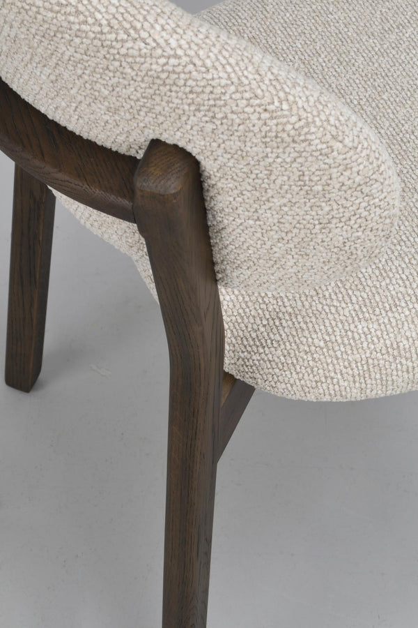 Närbild av en stol med cremefärgad stickad klädsel och mörkbruna träben i rustik finish