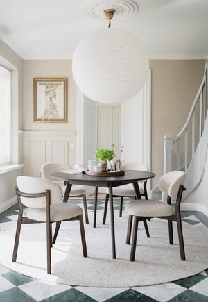 Matgrupp med runt bord och fyra stolar i beige tyg, stor vit taklampa och elegant inredning