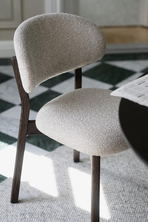 Stol med beige klädsel och mörkbruna träben på rutmönstrad matta i vardagsrum