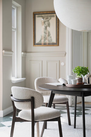 Matgrupp med runda stolar i beige tyg och runt svart bord under vit taklampa i ljust matrum