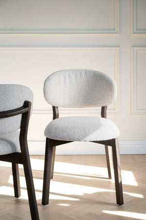 Stoppad stol med grå klädsel och mörka träben mot vit vägg med taklist