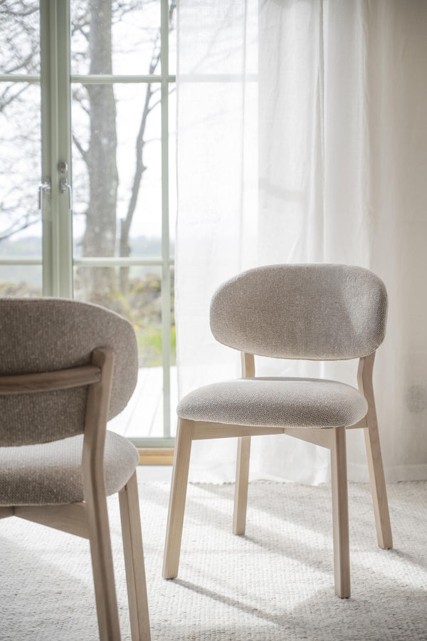 Beige stoppad matstol med träben framför fönster med gardin i ljust och luftigt rum