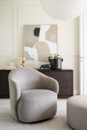 Grå rund fåtölj med matchande pall framför mörk sideboard med abstrakt tavla och dekoration