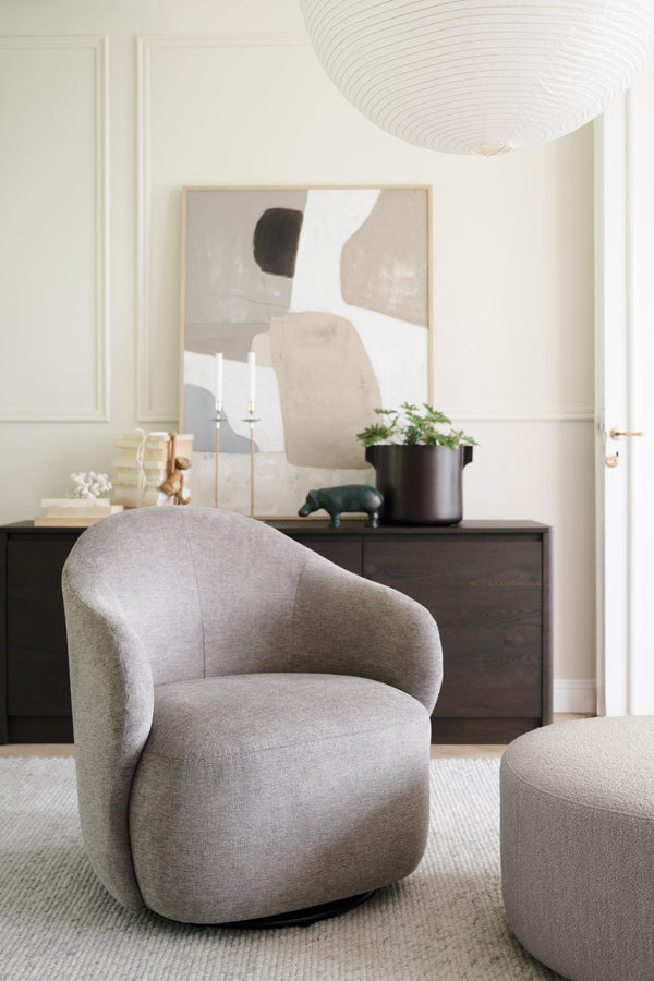 Grå rund fåtölj med matchande pall framför mörk sideboard med abstrakt tavla och dekoration