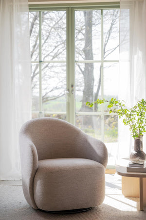 Beige bouclé fåtölj vid fönster med transparenta gardiner och gröna karmar, bredvid runt träbord med glasvas