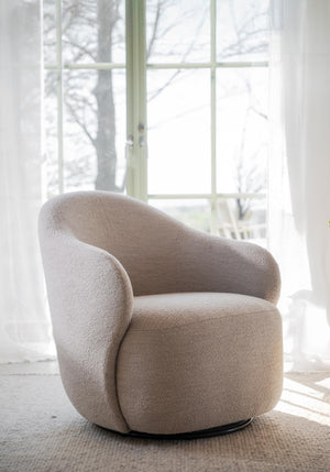 Beige snurrfåtölj i bouclé med rundad design vid fönster i ljust rum