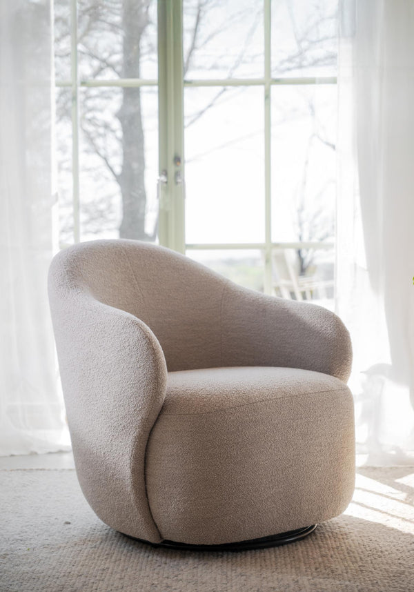 Beige snurrfåtölj i bouclé med rundad design vid fönster i ljust rum