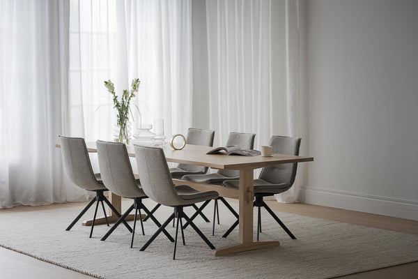 Matgrupp med ljust trä och sex grå stolar med svarta ben i minimalistisk matsal med vita gardiner