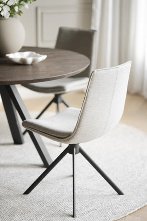 Modernt matbord med grå träskiva och svarta metallben, omgivet av ljusgrå stopade stolar med svart stativ
