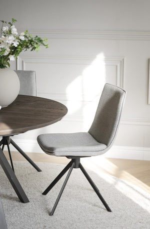 Grå stoppad matstol med svarta ben vid runt matbord i ljus matsal med blommor