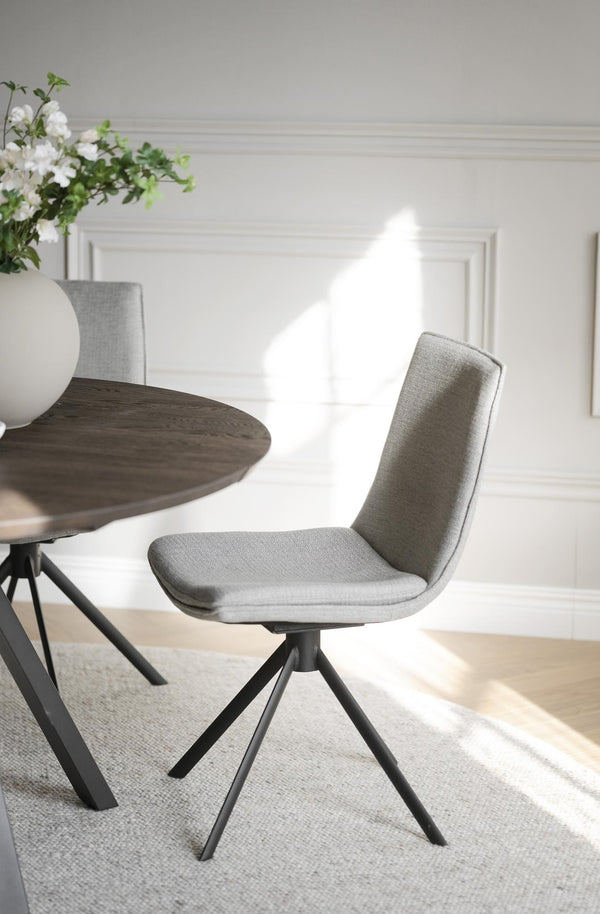 Grå stoppad matstol med svarta ben vid runt matbord i ljus matsal med blommor