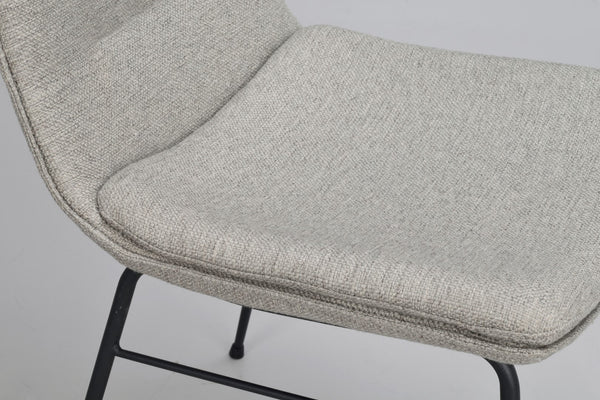 Närbild på sits i ljusgrå textil med svarta metallben på stol