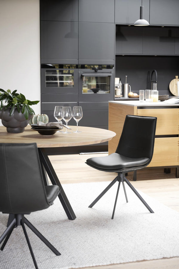 Modern matgrupp med runt träbord och svarta stolar i elegant kök med grå skåp och trädetaljer