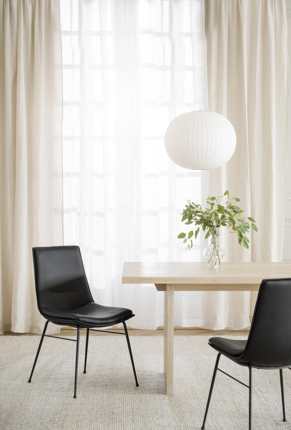 Matgrupp med ljust träbord, svarta stolar och vit taklampa i minimalistisk skandinavisk matsal