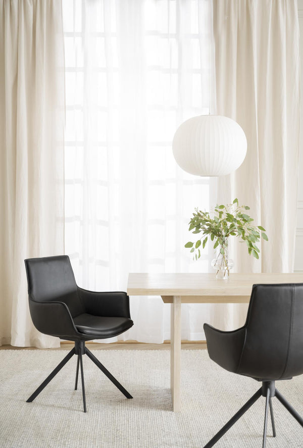 Svarta lädermatbordsstolar med svängbar funktion vid ljust matbord med vit taklampa och gardin i bakgrunden