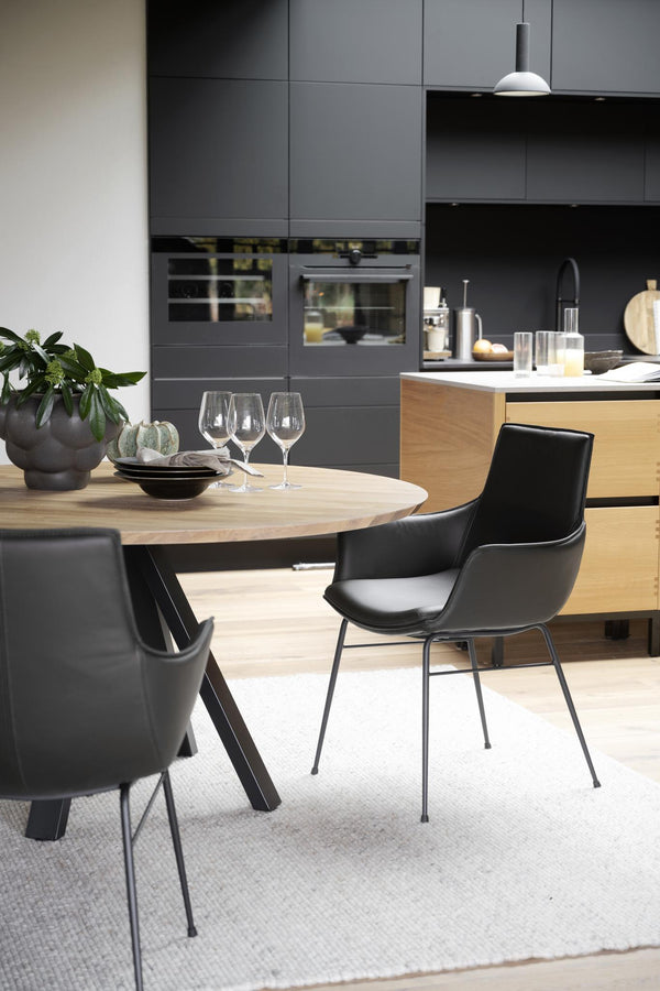 Modern matplats med runt träbord, svarta stolar och grått kök med trädetaljer i öppen planlösning