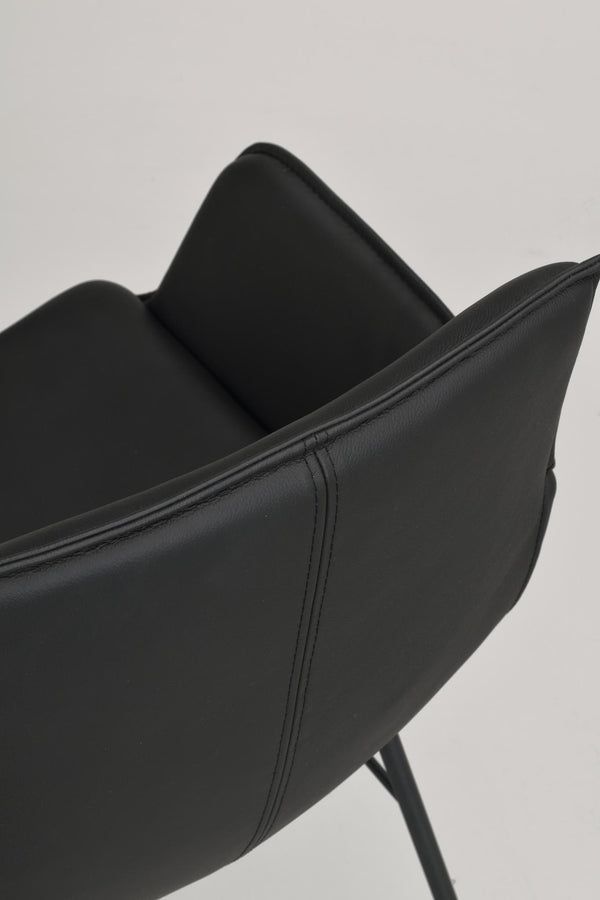 Närbild på svart fåtölj i konstläder med synlig sömdetalj och kudde