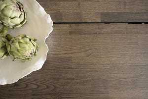 Vit serveringsfat med krusad kant och två kronärtskockor på mörkt trägolv