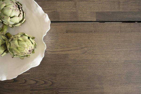 Vit serveringsfat med krusad kant och två kronärtskockor på mörkt trägolv