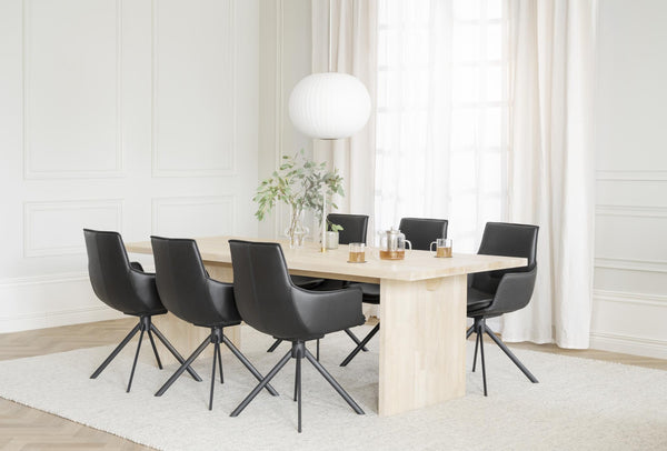 Matgrupp med ljust träbord och sex svarta stolar i modern matsal med vita väggar