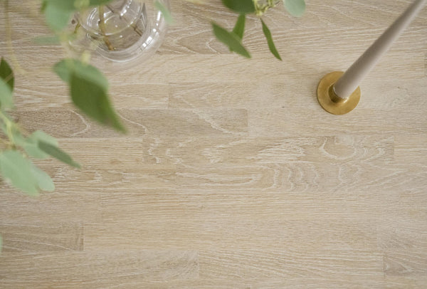 Ljust trägolv med glasvas, gröna växtskott och beige mortel och stöt i mässing