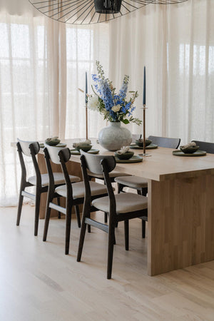 Matbord i trä med stolar, vacker blomsteruppsättning och elegant bordsdukning i ljus matsal