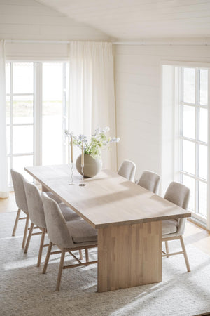 Ljust matrum med träbord, beiga stoppade stolar och stora fönster med vita gardiner i minimalistisk skandinavisk stil