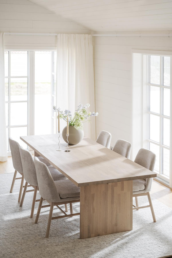 Ljust matrum med träbord, beiga stoppade stolar och stora fönster med vita gardiner i minimalistisk skandinavisk stil