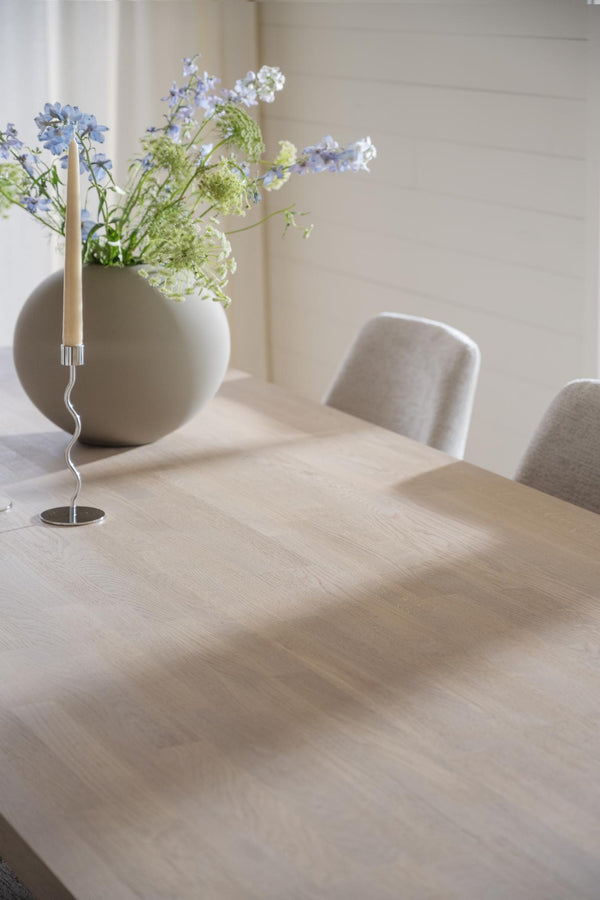 Ljus beige träbord med vit vas fylld med blå och vita blommor, samt ett dekorativt ljusstake med vridna detaljer